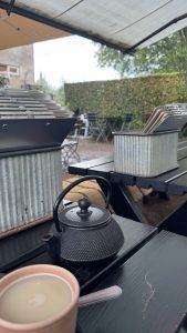 Outdoor café tables under a large umbrella during summer rain.