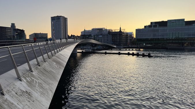 Modern pedestrian bridge curving across the canal at sunset.